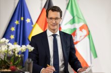 Ministerpräsident Hendrik Wüst sitzt vor Flaggen am Schreibtisch
