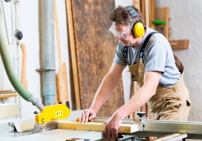 Das Bild zeigt einen Handwerker an einer industriellen Holzschneidemaschine.
