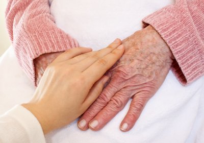 Bild auf dem eine Pflegerin die Hände einer älteren Frau streichelt