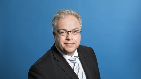 Staatssekretär Dr. Patrick Opdenhövel freundlich lächelnd vor blauem Hintergrund.
