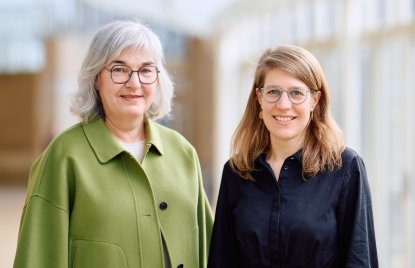 Petra Ladenburger, eine ältere Frau mit grauen schulterlangen Haaren und einer runden Brill in grünem Kostüm steht links neben Verena Schäffer in einem schwarzen Hemd