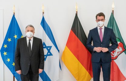 Zwei Männer stehen vor den Flaggen der EU, Israel, Deutschland und NRW