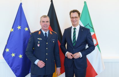 Generalleutnant Gerald Funke steht im Bundeswehr-Uniform links neben Ministerpräsident Wüst im Anzug. Hinter ihnen die Flaggen der europäischen Union, Deutschlands sowie von Nordrhein-Westfalen