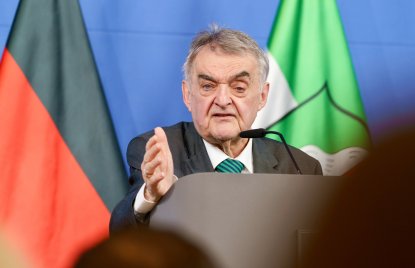 Minister Reul spricht an einem Rednerpult vor Flaggen