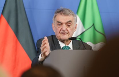 Minister Reul spricht an einem Rednerpult vor Flaggen