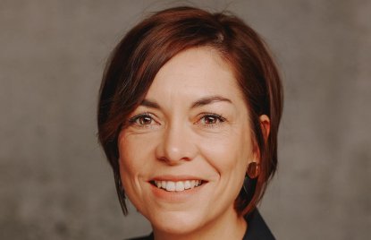 Eine Frau mit kurzen braunen Haaren, braunen Augen, in schwarzem Blazer lächelt in die Kamera