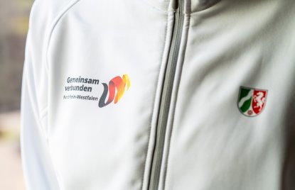Ein Close-Up einer weißen Sportjacke mit dem NRW-Wappen und dem Logo von Gemeinsam verbunden