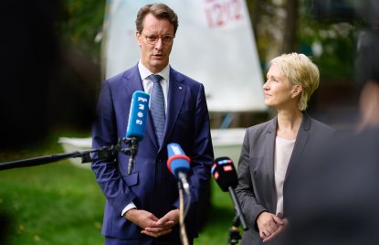 MP WÜst und MP Schwesig geben eine Statement auf einer Wiese, im Hintergrund ein Segelboot