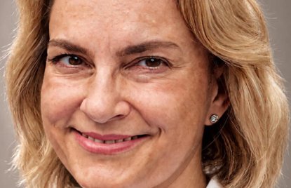 Eine blonde Frau in weißem Blazer lächelt in die Kamera