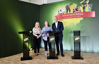 zwei Frauen und ein Mann stehen hinter drei Pulten vor einer grünen Leinwand mit einem EhrenamtAtlas Schriftzug