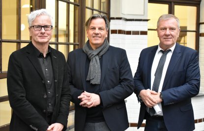 drei Männer stehen vor einer weißen Säule und hell beleuchtetem Hintergrund