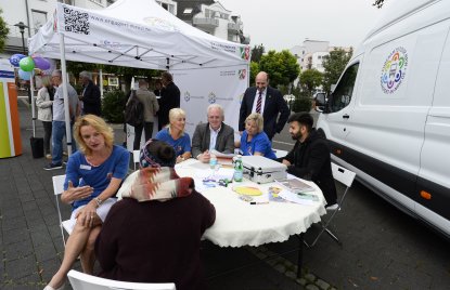 Ehrenamtstour-Veranstaltung: Eine Gruppe sitzt an einem runden Tisch, rechts steht der Ehrenamtstourbus, hinten steht ein Pavillonzelt.