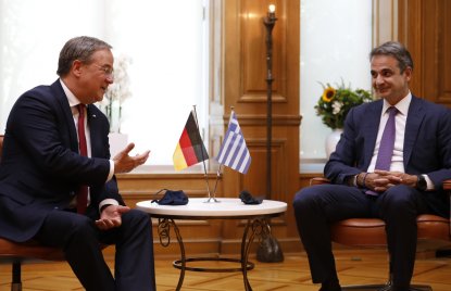 Zwei Männer sitzen neben einem Tisch auf dem eine Fahne von Deutschland und Griechenland stehen