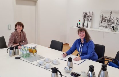 Staatssekretärin Andrea Milz in blauer Strickjacke sitzt mit einer Dame der Stadt Köln an einem Tisch.