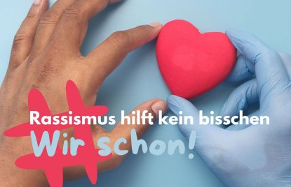 Eine dunkelhäutige Hand links sowie eine Hand in blauem Einweghandschuh rechts halten zusammen ein rotes Herz (blauer Hintergrund), darauf der Slogan der Kampange #RassismusHilfKeinBisschen - Wir schon!