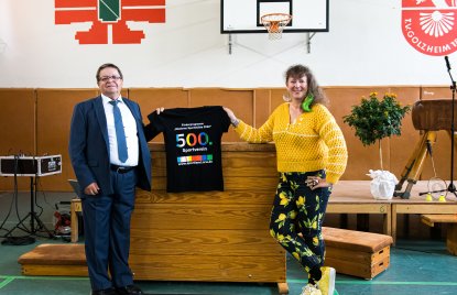 Staatssekretärin MIlz hält ein schwarzes T-Shirt mit Logo der Förderung mit der Zahl 500 in Regenbogenfarben.