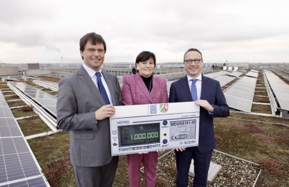 Drei Personen stehen auf einem Dach vor einer großen Solar-Anlage und halten gemeinsam einen Scheck hoch