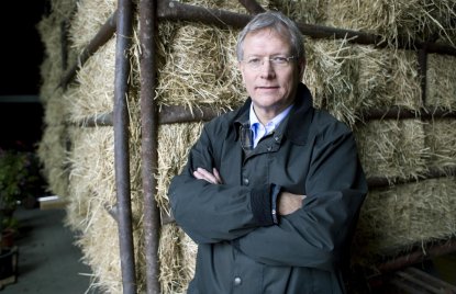 Eckhard Uhlenberg in dunkler Jacke mit verschränkten Armen vor Heuballen stehend.
