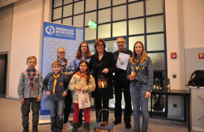 Auf dem Foto ist Ministerin Ute Schäfer gemeinsam mit Kindern und Jugendlichen zu sehen, die das Friedenslicht aus Betlehem überreichen.