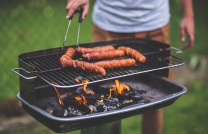 Ein Mann dreht Würste auf einem Grill im Garten