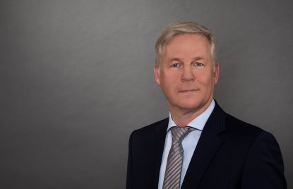 Ein Mann mit hellen Haaren, blauem Jackett, hellblauem Hemd und grau-blau gestreifter Kravatte