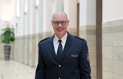 Dirk Hulverscheidt, der neue Inspekteur der Polizei NRW steht in blauem Polizeianzug lächelnd in einer Halle. Auf dem Bild ist nur sein Oberkörper zu sehen mit dunkelblauem Sakko, weißem Hemd und blauer Krawatte. Er trägt eine Brille und hat sehr kurz geschnittene Haare.