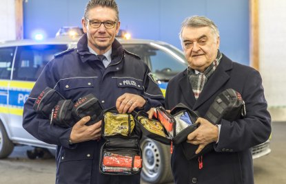 Minister Reul überreicht Medipacks an Dietmar Henning von der Polizei Düsseldorf. Im Hintergurnd steht ein Polizeiwagen.