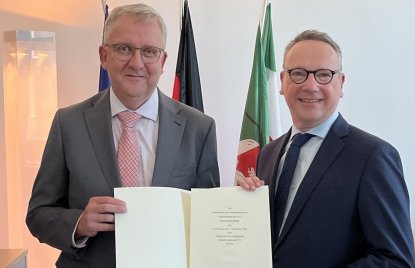 Minister Dr. Limbach rechts im schwarzen Anzug übergibt Klaus Georg Müller im grauen Anzug mit roter Krawatte eine Urkunde
