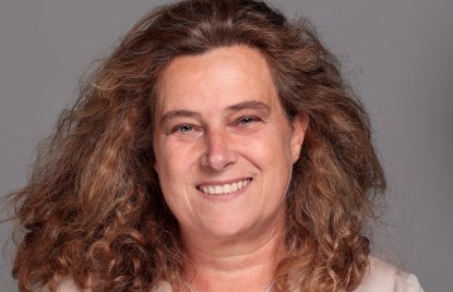 eine Frau mit offenen Haaren, Bluse und Blazer lächelt frontal in die Kamera