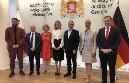 vier Männer und drei Frauen stehen vor einer Wand mit dem georgischen Wappen und einer Deutschland-Fahne