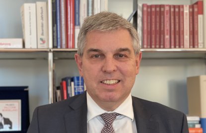 ein grauhaariger Mann mit Anzug und Krawatte vor einem Bücherregal