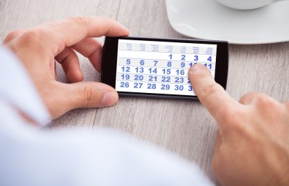 Eine Hand hält ein Smartphone mit einem Kalender auf dem Bildschirm, mit einem Zeigefinder auf dem Display 