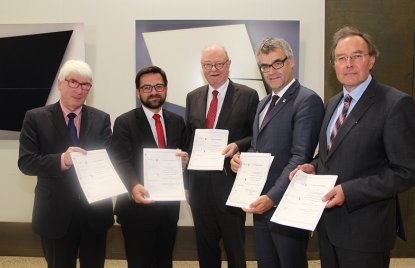 Die Vertreter schauen in die Kamera und halten jeweils den Kooperationsvertrag in den Händen