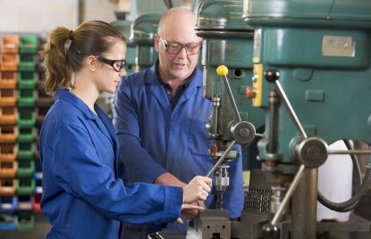 Auf diesem Foto zu erkennen sind ein weiblicher Lehrling mit Ausbilder an einer Maschine