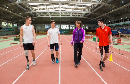 4 Sportler auf einer roten Tartanbahn. 3 von ihnen haben je eine Beinprothese.