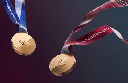 zwei Goldmedaillen der olympischen Winterspiele in Mailand. Zu sehen sind auf beiden die 5 olympischen Ringe auf Gold, die linke Medaille hat ein blau-weißes Band, die recht ein rot-weißes.