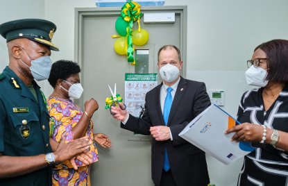 Zwei Männer und zwei Frauen stehen vor einer Tür, die mit gelben und grünen Ballons geschmückt ist. Minister Stamp hält eine ebenfalls verzierte Schere