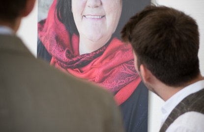 Fotoausstellung an einer Wand zeigt eine obdachlose Frau mit einem roten Schal als beeindruckenden Porträtbild.