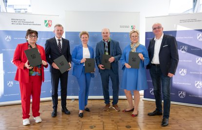 vor blau-weißen Roll-Ups der Ministeriums für Kultur und Wissenschaft sowie der Ministeriums der Finanzen stehen von links nach rechts nebeneinander Gabriele Willems, BLB NRW-Geschäftsführerin, Dr. Dirk Günnewig, Staatssekretär im Ministerium der Finanzen, Ina Brandes, Ministerin für Kultur und Wissenschaft, Prof. Dr. Ulrich Rüdiger, Rektor RWTH Aachen. Prof. Dr. Tamara Appel, Rektorin der FH Dortmund, Prof. Dr. Manfred Bayer, Rektor der TU Dortmund