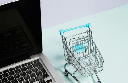 Neben einem Laptop steht ein Miniatur-Einkaufswagen