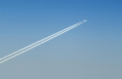 Flugzeug hoch oben am blauen Himmel, mit Kondesstreifen hinter sich