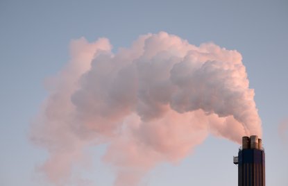 Rauch, der aus einem Industrieschornstein gegen einen klaren Himmel aufsteigt und die Verschmutzung veranschaulicht.