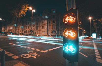 Kreuzung mit beleuchteter Fahrradampel im Fokus, bei Nacht, Verkehr nur als leuchtende Linien im Hintergrund