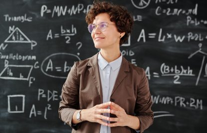 eine Frau in braunem Blazer vor einer Tafel voller mathematischer Formeln