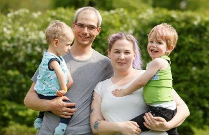 Familie Reinhold - Vater und Mutter halten jeweils einen Sohn auf dem Arm. Alle lächeln.