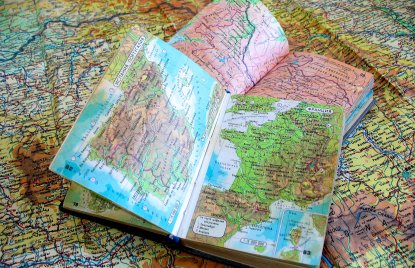 2 aufgeschlagene Landkartenbücher liegen auf einer großen Landkarte, die sich über das gesamte Bild erstreckt.