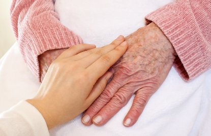 Bild auf dem eine Pflegerin die Hände einer älteren Frau streichelt