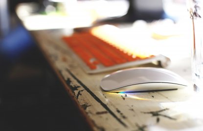 Orangene Tastatur und Maus auf einem Tisch im Sonnenschein