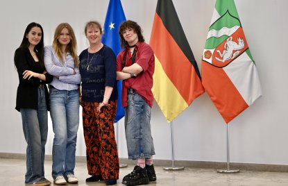 vier Frauen, davon drei mit verschränkten Armen, stehen vor den Flaggen von Europa, Deutschland und NRW 