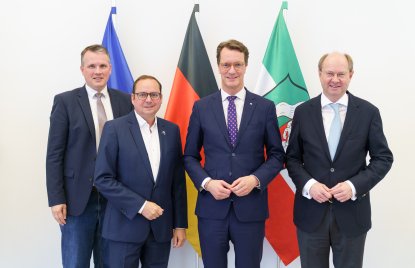 Von links nach rechts stehen Bürgermeister Tobias Stockhoff, Oberbürgermeister Thomas Kufen, Ministerpräsident Hendrik Wüst und Landrat Dr. Olaf Gericke gemeinsam vor den Flaggen der Europäischen Union, Deutschlands und Nordrhein-Westfalens. Die vier Politiker tragen dunkle Anzüge und blicken in die Kamera.